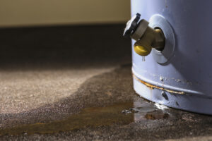 Water leaking from the plastic faucet on a residential electric water heater sitting on a concrete floor.