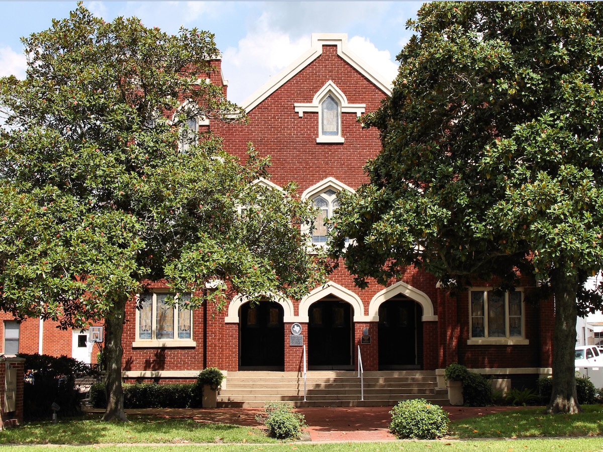 Termite Control Service in Richmond, Texas Red brick building framed by two large trees, with arched doorways and steps leading up to the entrance