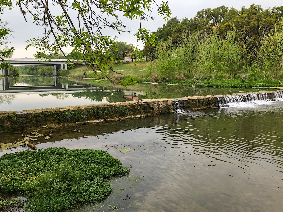 Termite Control Service in Salado, Texas Small waterfall and calm river with greenery and a bridge in the background