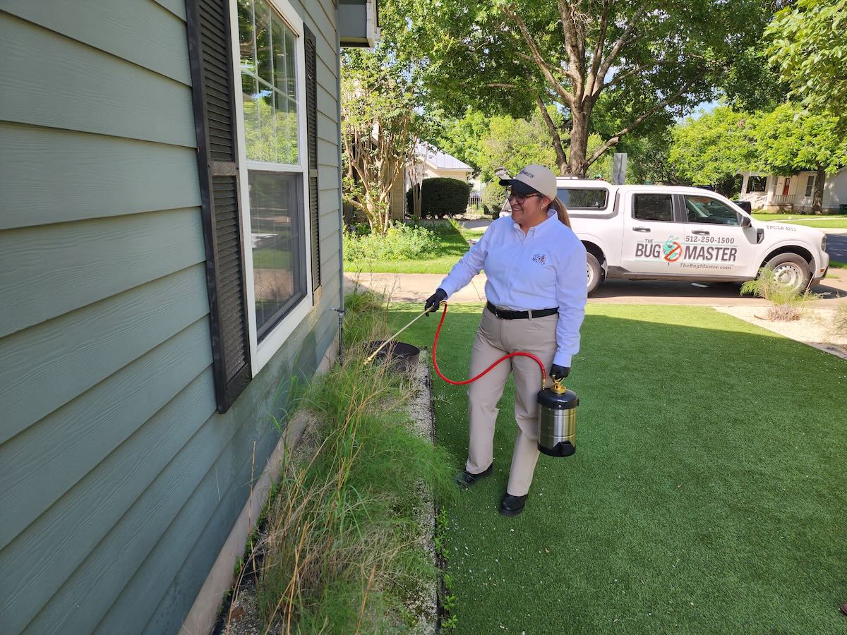 Professional Preventive Pest Control in Action A certified Bug Master technician applies preventive pest control treatment around a home’s foundation, with a company truck parked nearby.